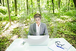 Portrait of young handsome business man in suit working at laptop at office table in green forest park. Business concept.