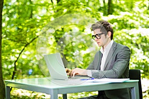 Portrait of young handsome business man working at laptop at office table in green park. Business concept.