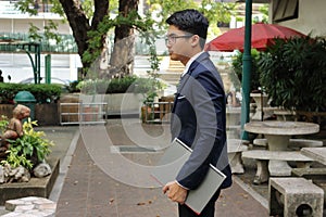 Portrait of young handsome businessman is holding a laptop on his hands in nature blurred background.