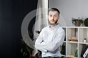 Portrait of a young handsome Caucasian brunette man with a beard. 20-25 years old standing in plaid shirt. Hands folded on his