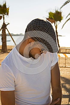 Portrait of young handsome Caucasian male with glasses and cap and toothpick in the mouth on beach