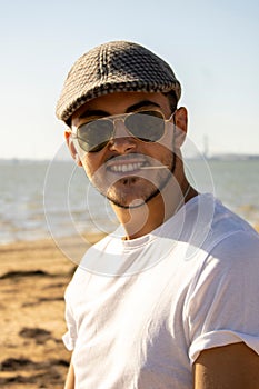 Portrait of young handsome Caucasian male with glasses and cap and toothpick in the mouth on beach