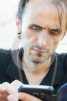 Portrait of a young, handsome, Caucasian man with stubbly beard using smart phone