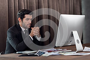 Portrait of young handsome confident businessman in suit working with desktop computer at office