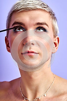 portrait of young, handsome gay man applying make-up, eyelashes mascara isolated