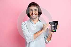 Portrait of young handsome happy cheerful man male guy use credit card terminal paypass wear glasses isolated on pink