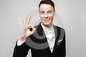 Portrait of a young handsome happy man, in a business suit, smiling, and showing an OK gesture, on gray background.