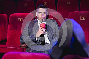 Portrait of a young, handsome man alone in a movie theater in a business suit, with his feet on the front seat and