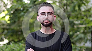 Portrait of young handsome man with beard and glasses. Young man in black shirt smiling looking at camera. Outdoor nature backgrou