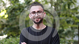 Portrait of young handsome man with beard and glasses. Young man in black shirt smiling looking at camera. Outdoor nature backgrou
