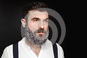 Portrait of young handsome man with beard in snow over black background.