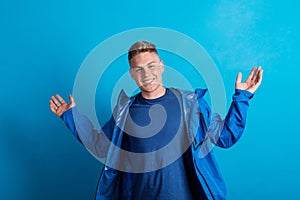 Portrait of a young man with blue anorak in a studio, standing against blue background. photo