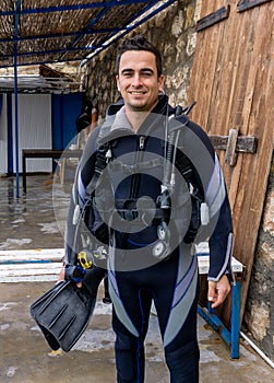 Portrait of a young handsome man diver ready to go scuba diving with cold water wet suit, fins, buoyancy compensator