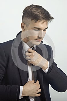 Portrait of young handsome man fixing his black tie. Wearing classic black suit and white shirt, official style, serious look.