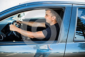 Portrait of young handsome man in his new silver gray car, relaxing, hand on steering wheel, on outdoors background with