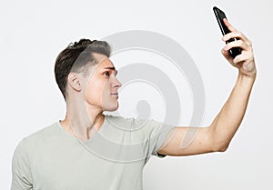 Portrait of a young handsome man in a t-shirt, taking a selfie, holding a phone