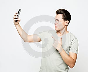 Portrait of a young handsome man in a t-shirt, taking a selfie, holding a phone