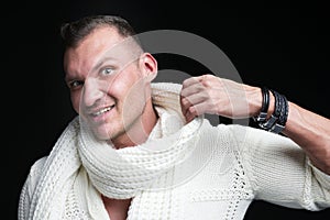 Portrait of young handsome man, wearing white sweater and scarf, isolated on dark studio background