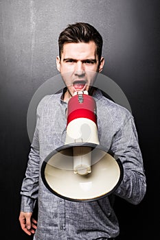 Portrait of young handsome man yelling into the megaphone over black background