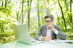 Portrait of young handsome manager in suit working at laptop at office in green forest park. Business concept.