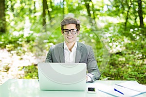 Portrait of young handsome manager working at laptop at office table in green park. Business concept.