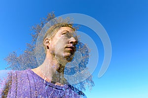 Double exposure of young handsome man and oak tree overlaying against blue sky