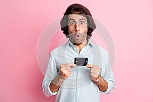 Portrait of young handsome shocked amazed man male guy with open mouth hold credit card wear glasses isolated on pink