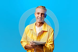 Portrait of young handsome smiling guy, student in bright fashion outfit holding tablet looking at camera isolated on