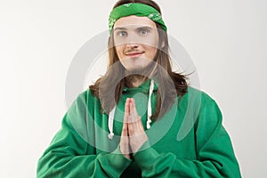 Portrait of young handsome smiling happy man in green hoodie looking at the camera and showing namaste agains white background.