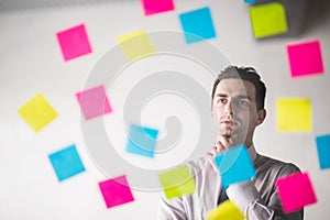 Portrait of young handsome start-up businessman thinking on sticky notes and looking straight at camera