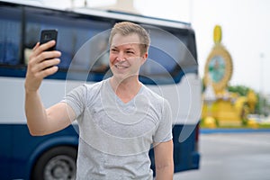 Young happy tourist man taking selfie against Ratchadamnoen street in Bangkok photo