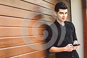 Portrait of young handsome Turkish male model. Mediterranean race brunette in black shirt is using a hand phone of a