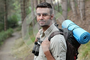 Portrait of a young handsome wanderer man with backpack goes down the road with copy space, happy hiker walking lonely in mountain