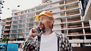 Portrait of young handyman making call while standing at construction area. Engineer talking on the phone on a construction site.