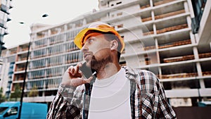 Portrait of young handyman making call while standing at construction area. Engineer talking on the phone on a construction site.