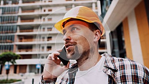 Portrait of young handyman making call while standing at construction area. Engineer talking on the phone on a construction site.