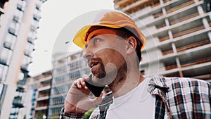 Portrait of young handyman making call while standing at construction area. Engineer talking on the phone on a construction site.