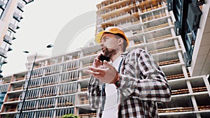 Portrait of young handyman making call while standing at construction area. Engineer talking on the phone on a construction site.