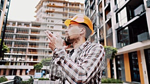 Portrait of young handyman making call while standing at construction area. Engineer talking on the phone on a construction site.