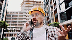 Portrait of young handyman making call while standing at construction area. Engineer talking on the phone on a construction site.