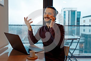 Portrait of young happiness attractive man talking on smartphone, working at laptop, background of panoramic windows