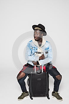 Portrait of young happy african man sitting on suitcase isolated on white background