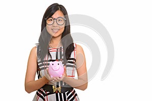 Portrait of young happy Asian businesswoman holding piggy bank