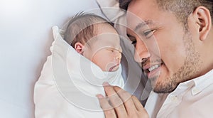 Portrait of young happy asian father with his newborn baby, copy space with bed in the hospital background.