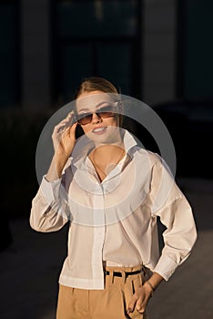Portrait of a young, happy and attractive Caucasian woman in casual clothes and sunglasses while walking around the city. The