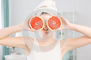 Portrait of young happy beautiful woman with healthy perfect smooth skin holds two pieces of grapefruit, closing two