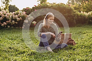 Portrait of young happy blonde woman listening to music with headphones and smiling on a green grass outdoor. Music