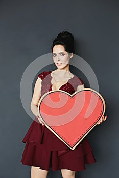 Portrait of a young happy brunette woman in red dress with a big red paper heart in her hands with copy space for your