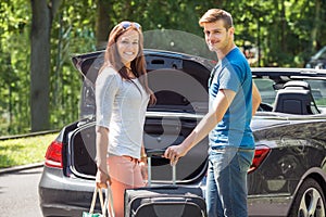 Smiling Couple Putting Luggage In A Car Trunk