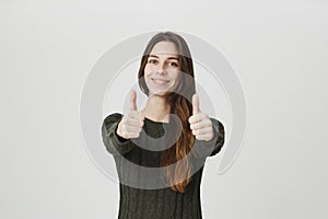 Portrait of young happy european girl showing her thumbs up in approving gesture looking cheerful, isolated over white